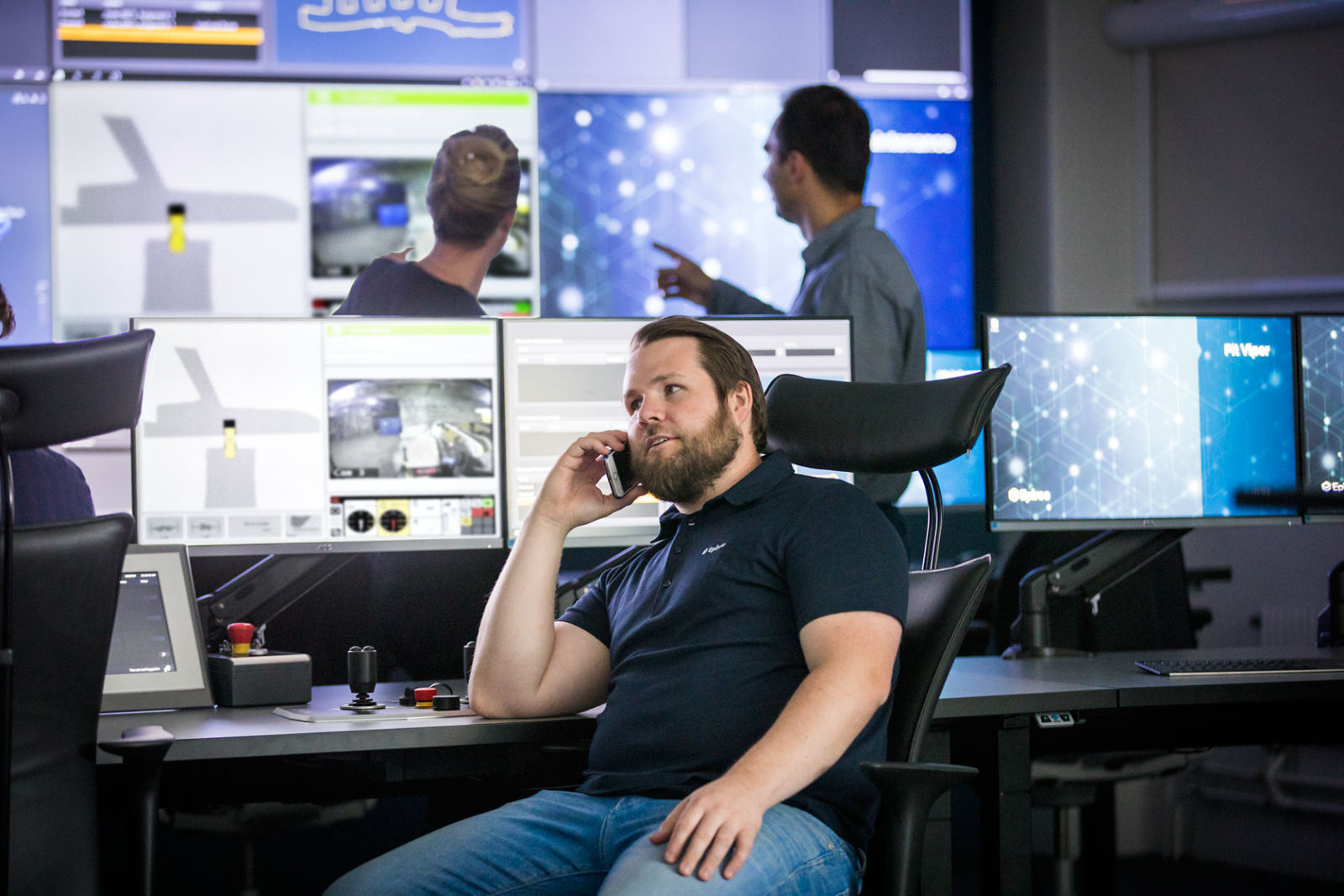 Male office employee talking on cell phone in front of large computer screens in Epiroc Control Tower