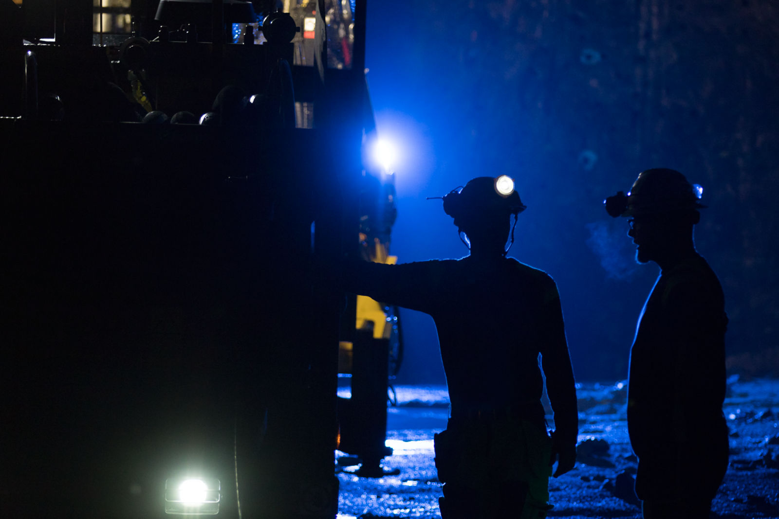 Operators with hardhats standing next to a Simba E6W long-hole drill rig in blue backlight in underground mine
